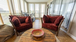A cozy room with two red velvet chairs, a woven basket on a wooden table, and large windows with blinds.