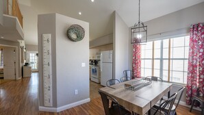 A spacious kitchen with a wooden dining table, chairs, and a hanging light fixture.