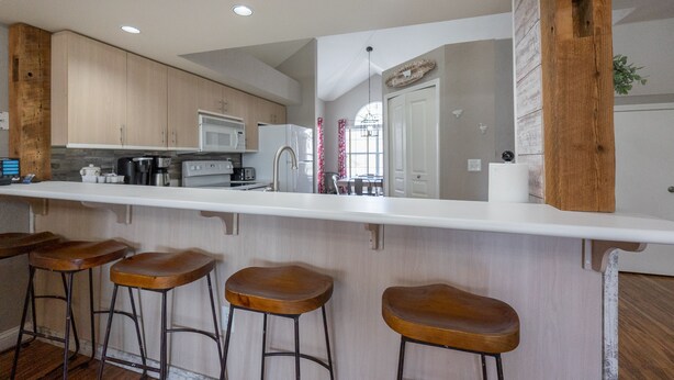 A modern kitchen with wooden cabinets, a white countertop, and three wooden bar stools.