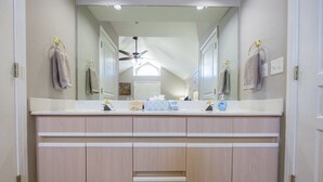 A bathroom with a large mirror, two sinks, a ceiling fan, and a towel rack.