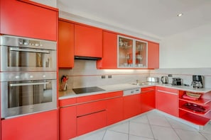 A modern kitchen with red cabinetry, stainless steel appliances, and a white countertop.