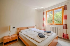 A bedroom with a wooden bed, a bedside table, a lamp, and a window with curtains.