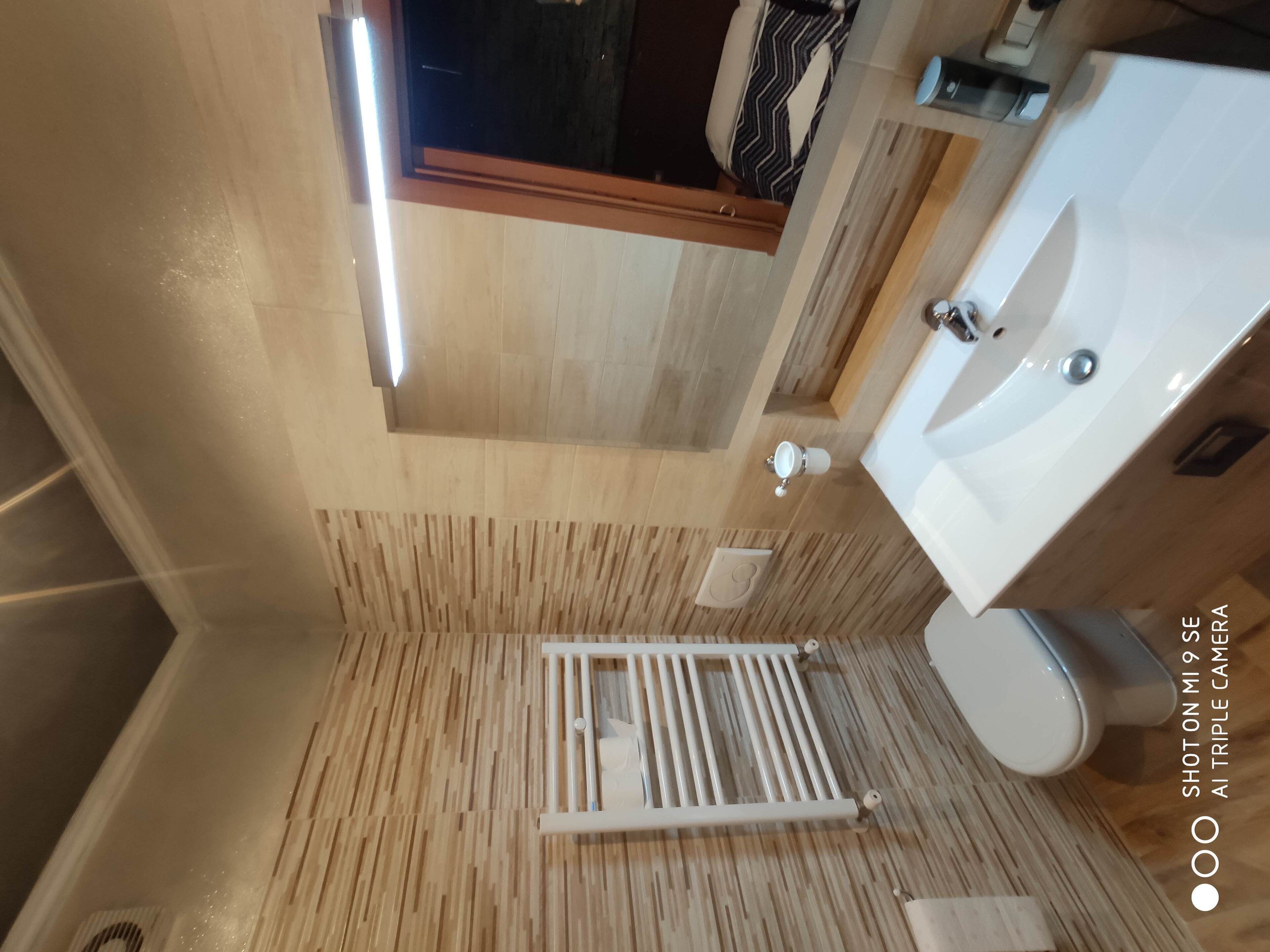 A compact bathroom with a wooden floor, a white radiator, a toilet, and a sink.