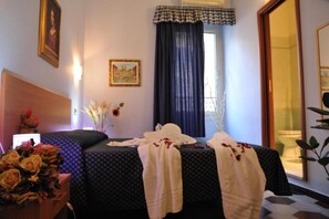 A hotel room with a bed, a nightstand with a vase of flowers, a painting on the wall, and a window with curtains. - Double B Carlo Alberto (Rome)