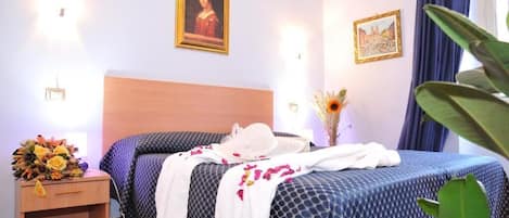 Una habitación de hotel con cama, mesita de noche con lámpara y un jarrón con flores.