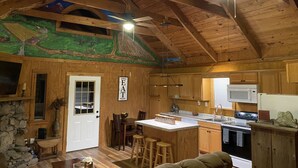 L’intérieur d’un chalet rustique comprend un coin repas, une cuisine et une fresque peinte au plafond.