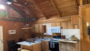 Une cuisine rustique avec des meubles en bois, un îlot central doté de tabourets, un four à micro-ondes, une cuisinière et un réfrigérateur.