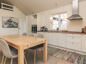 A modern kitchen with white cabinetry, a wooden dining table, and a large window providing natural light. - 5 Star Holiday Home in Nysted (Nysted)