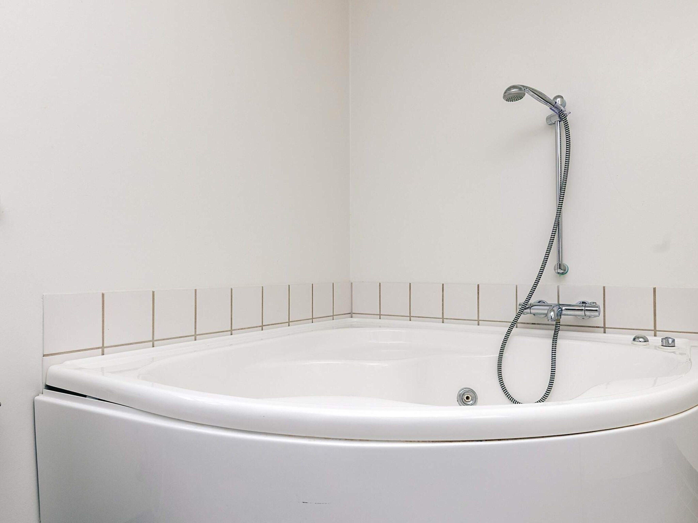 A white bathtub with a shower head and hose, set against a tiled wall.