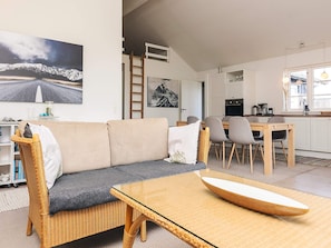 A modern living room with a sofa, a glass-top coffee table, and a dining area with chairs and a table.