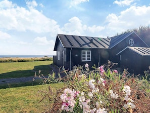 A black house with a window and a door, surrounded by a grassy field and flowers. - 5 Star Holiday Home in Nysted (Nysted)