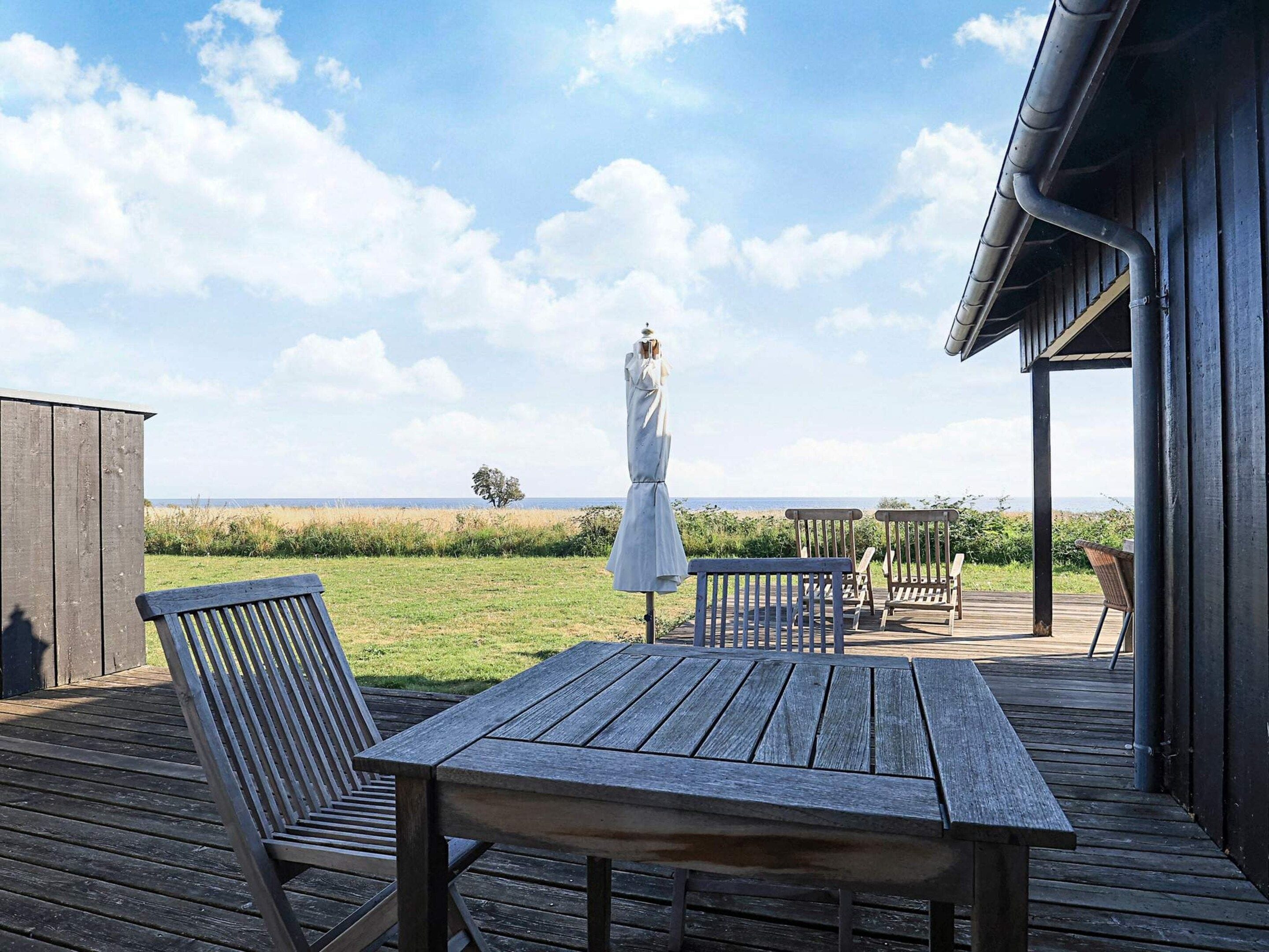 A wooden deck with a table and chairs, overlooking a grassy field and the sea.