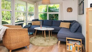 A cozy living room with a dark blue sofa, a wicker chair, a small round table, and a magazine rack. - 8 Person Holiday Home in Knebel-by Traum (Knebel)