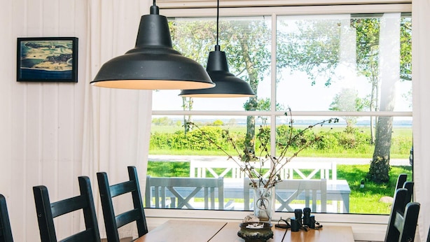 A dining area with a wooden table, black chairs, a vase with branches, and a view of greenery and a white fence outside. - 8 Person Holiday Home in Knebel-by Traum (Knebel)