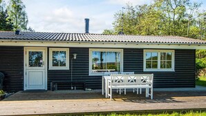 A small, single-story house with a dark exterior, a chimney, and a deck with outdoor furniture. - 8 Person Holiday Home in Knebel-by Traum (Knebel)