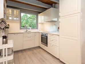 A kitchen with white cabinetry, a window with a view of greenery, a stainless steel oven, and a countertop with a coffee maker. - 5 Person Holiday Home in Ebeltoft (Ebeltoft)