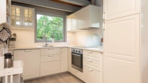A modern kitchen with white cabinetry, a built-in oven, and a window providing a view of trees. - 5 Person Holiday Home in Ebeltoft (Ebeltoft)