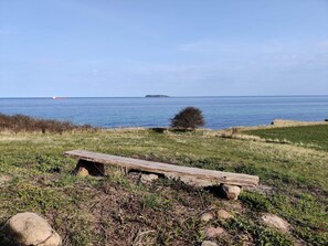 A wooden bench in a grassy area with a view of the sea and a distant island. - 5 Person Holiday Home in Ebeltoft (Ebeltoft)