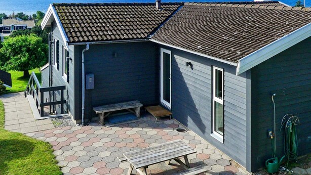 Una casa con techo de tejas, un banco de madera y un jardín con vistas al mar.