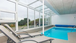 Una piscina con sillas de descanso y un área cubierta con amplios ventanales.