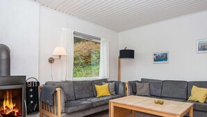 Una sala de estar acogedora con chimenea, sofás grises, una mesa de centro de madera y un ventanal con vistas al verdor.