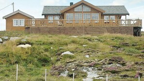 A two-story wooden cabin with a balcony, situated on a grassy hill with rocky terrain. - Holiday Home in Dyrvik (Frøya)