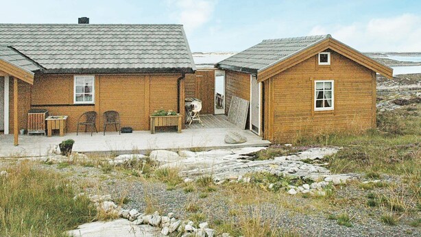 A wooden house with a tiled roof, a patio with chairs, and a view of the landscape.