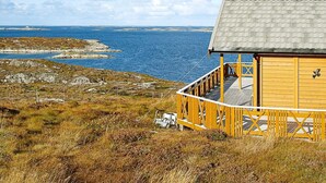 A wooden cabin with a balcony overlooking a coastal landscape.
