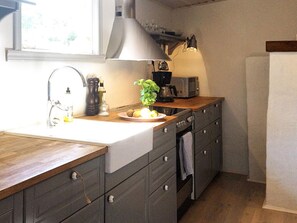 A kitchen with a wooden countertop, a sink, a stove, a microwave, and a window above the sink.