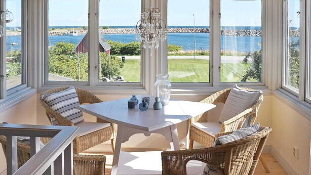 A sunroom with a view of the sea, wicker furniture, and a chandelier. - Holiday Home in Sölvesborg (Sölvesborg)
