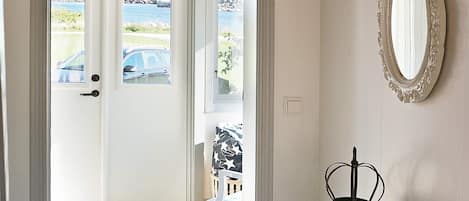 A room with a white door leading to a view of a body of water and parked cars. A black metal bucket is on a white surface.