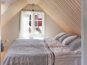 A bedroom with a sloped ceiling, a bed with patterned bedding, and a window with curtains. - Holiday Home in Sölvesborg (Sölvesborg)
