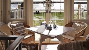A sunlit room with wicker furniture, a table with decorative items, and a view of a coastal area. - Holiday Home in Sölvesborg (Sölvesborg)