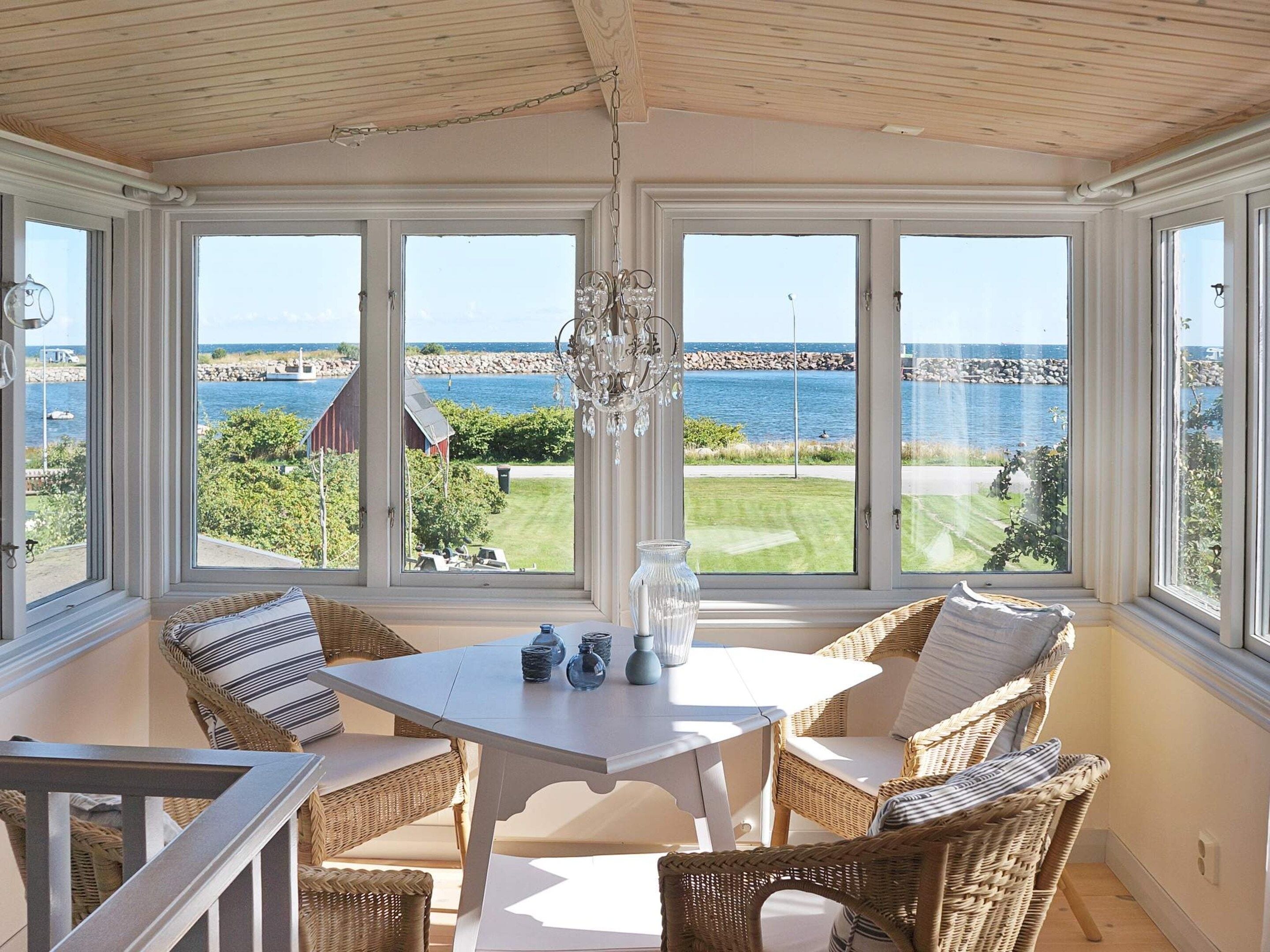 A sunroom with a view of the sea, featuring wicker furniture and a chandelier.