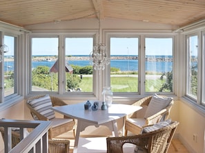 A sunroom with a view of the sea, featuring wicker furniture and a chandelier.