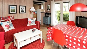 A cozy living room with a red sofa, a white coffee table, and a red and white polka dot tablecloth. There is a television and a red lamp in the room.