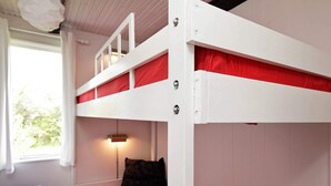 A bunk bed with red bedding, a small bedside table, and a lamp.