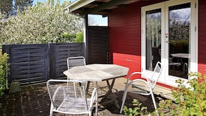 A patio with a table and two chairs, a red building, and a wooden fence.