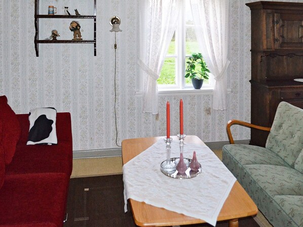 Un salon chaleureux avec un canapé rouge, un fauteuil vert, une table en bois ornée de bougies et une fenêtre avec une plante.