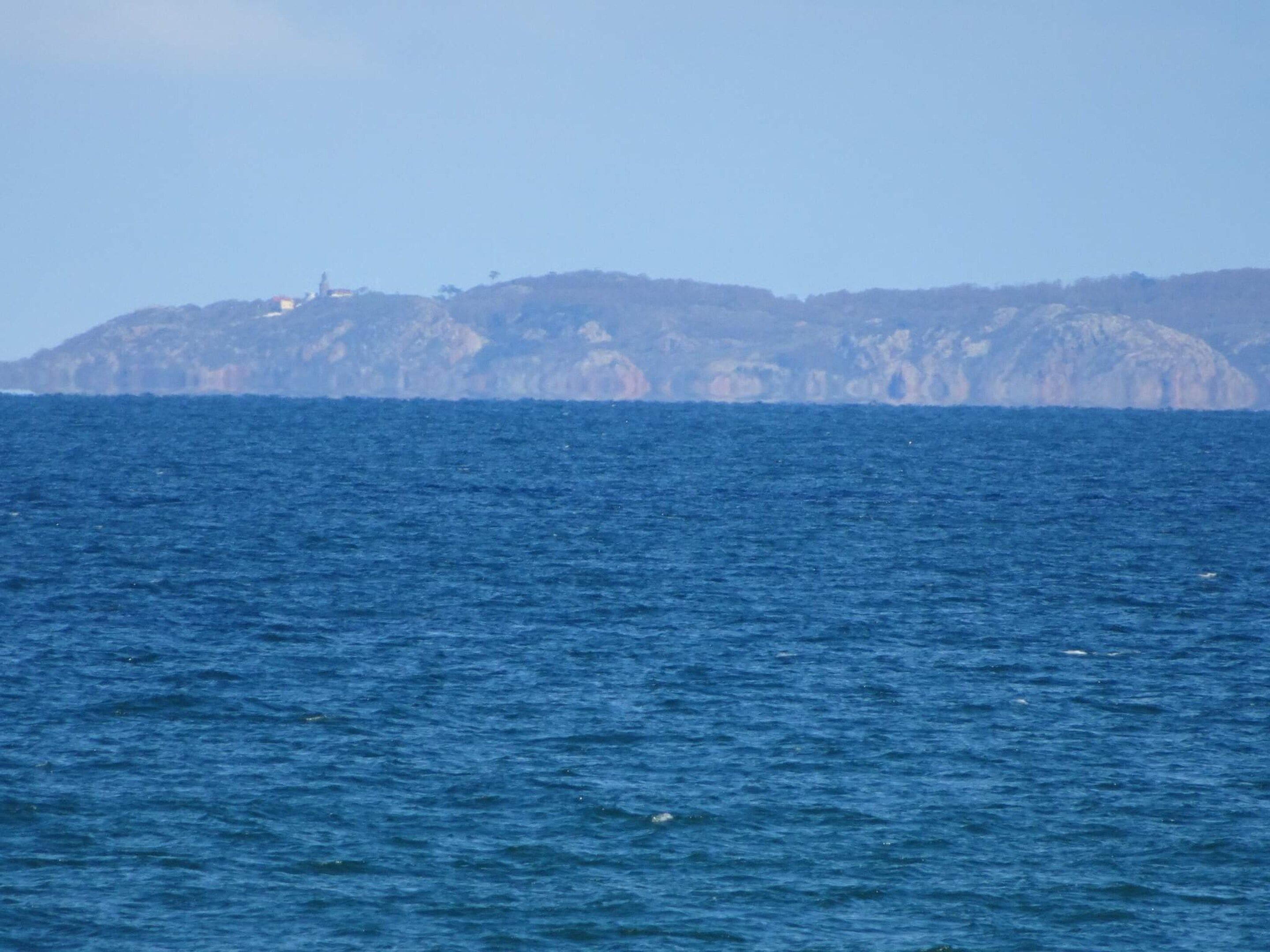 A view of a coastal area with a body of water and a distant landmass with a structure on top.