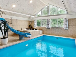 En indendørs swimmingpool med blå rutsjebane, bruseområde og store vinduer.