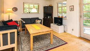 A cozy living room with a sofa, a wooden coffee table, a lamp, a TV, and a kitchen area with cabinets and a window. - Stylish Holiday Home in Hals near Sea (Hals)