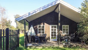A wooden cabin with a covered patio, a table with chairs, and a bicycle. - Stylish Holiday Home in Hals near Sea (Hals)