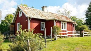 Ein rotes Bauernhaus mit weißem Tor und Fenstern, umgeben von einem weißen Zaun und viel Grün.