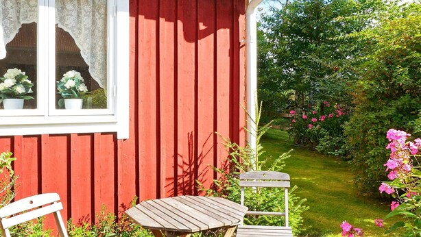 Ein rotes Holzgebäude mit einem Fenster, einem Holztisch und zwei Stühlen davor.