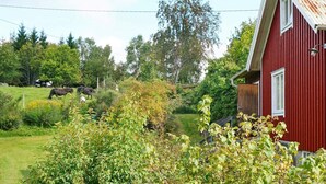 Ein roter Bauernhof mit einem weißen Fenster und einem Metalldach, umgeben von üppiger Vegetation und blauem Himmel.