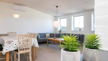 A dining area with a table and chairs, a sofa, and two potted plants.