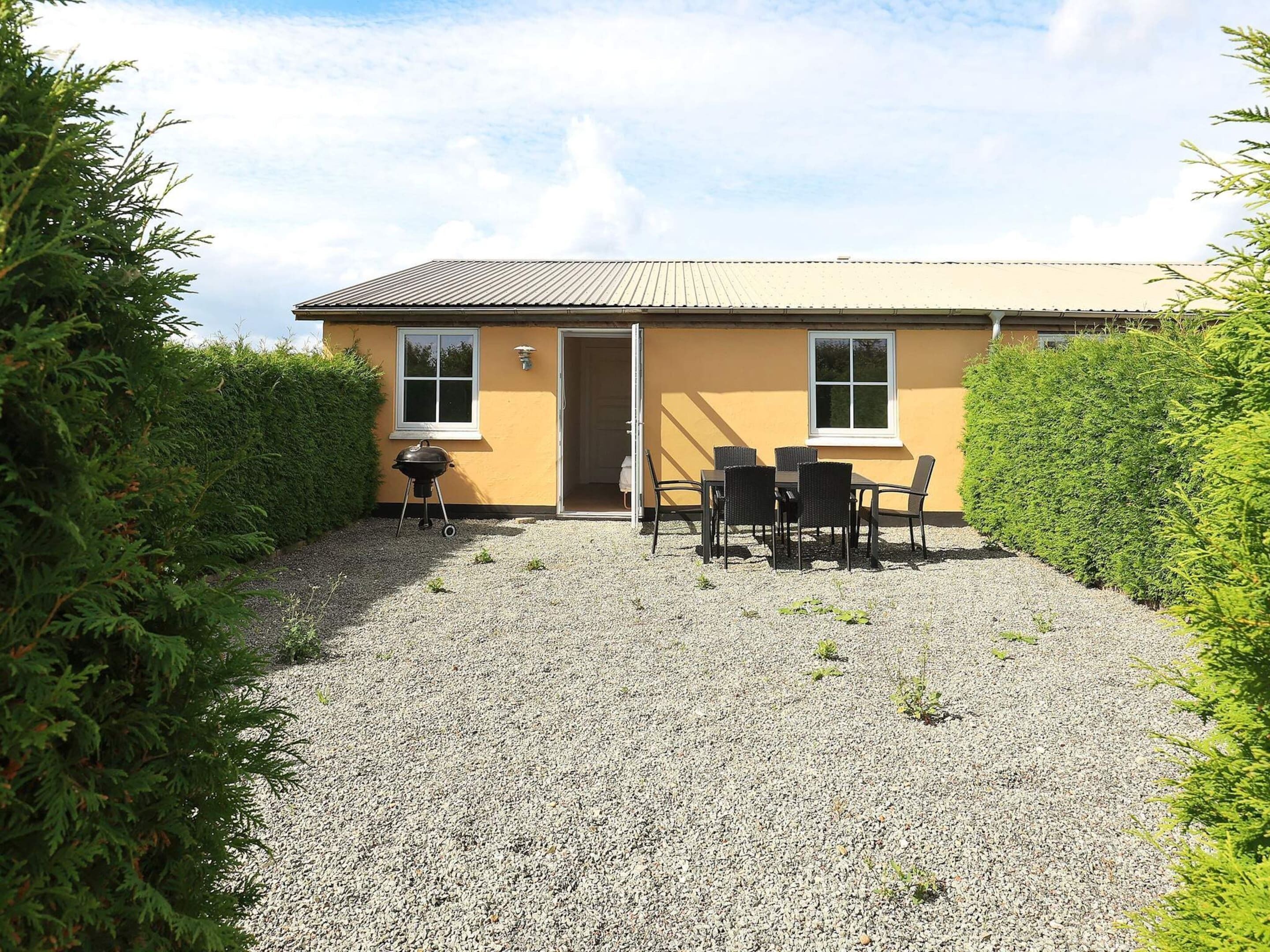 A yellow building with a gravel driveway, a door, and a table with chairs.