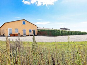 A single-story yellow building with a gravel driveway and a hedge in the background. - 6 Person Holiday Home in Faaborg (Faaborg)