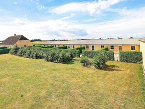 A large, yellow building with multiple windows and a flat roof, surrounded by well-maintained hedges and a grassy field. - 6 Person Holiday Home in Faaborg (Faaborg)